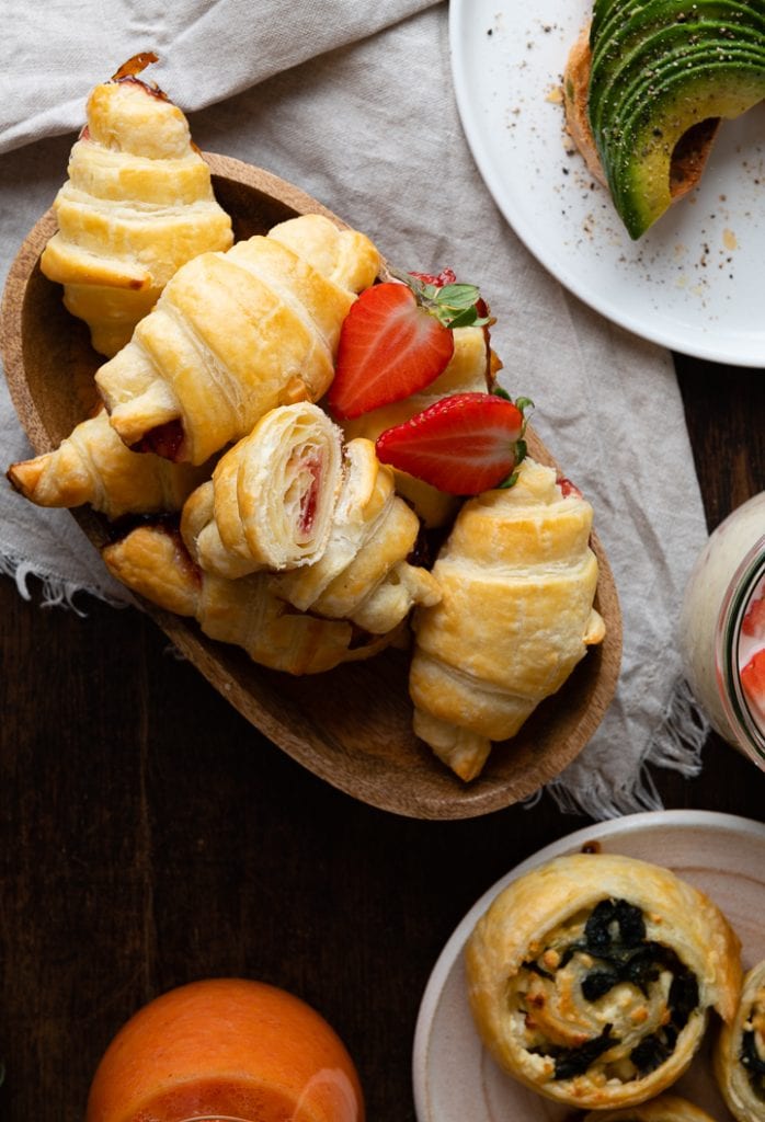 erdbeer croissant liegen auf dem Tisch, daneben sind blätterteigschnecken mit spinat und feta.