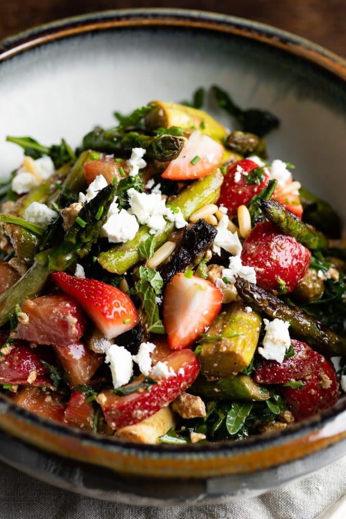 Salat mit grünem Spargel (geröstet), geschnittenen Erdbeeren, zerbröckeltem Feta-Käse und Pinienkernen, garniert mit Kräutern.