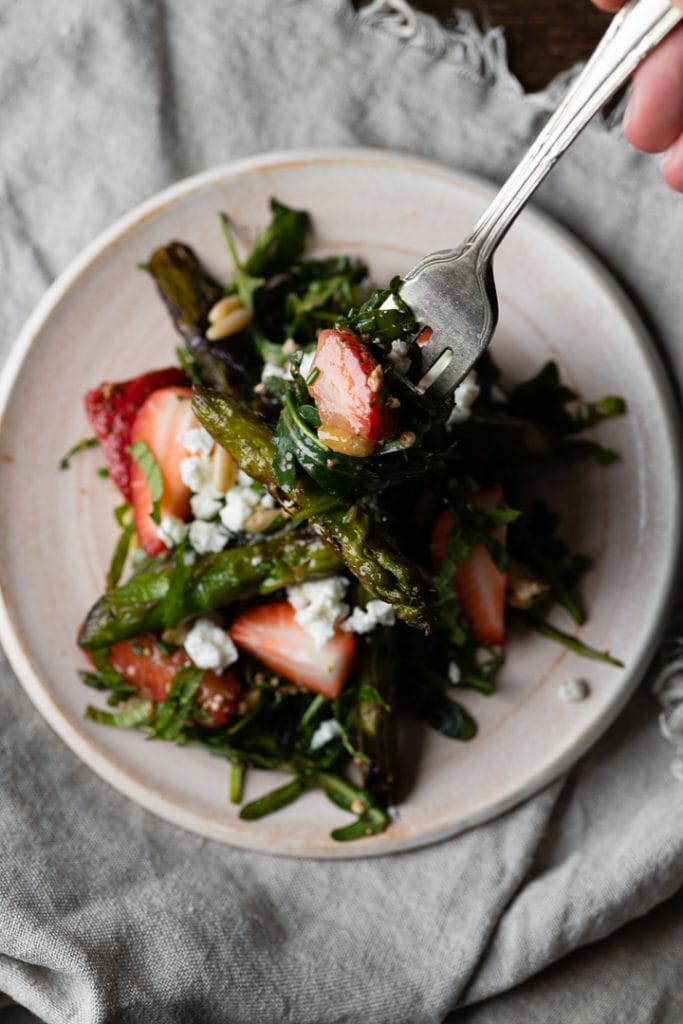 Eine Gabel nimmt grünen Spargel, eine Erdbeere und Salat.
