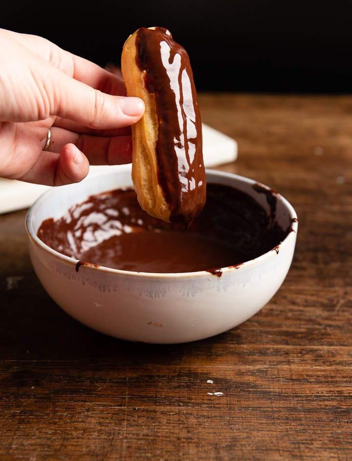 Ein französisches eclairs wird in Schokolade eingetaucht.