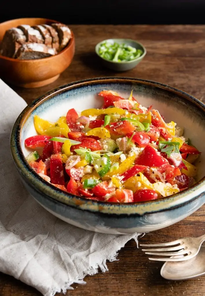 Gewürfelter Paprikasalat aus roter und gelber Paprika mit Feta und gehackten Frühlingszwiebeln in einer blauen Schale.
