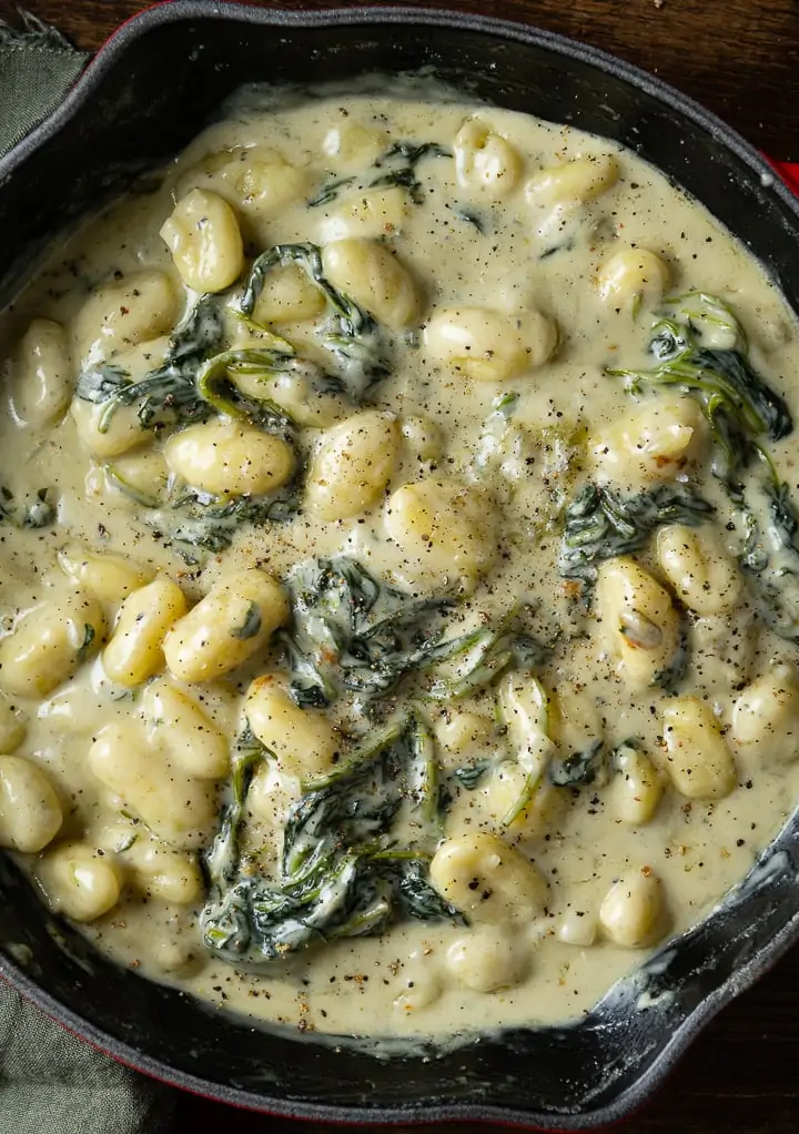 Gnocchi in cremiger Gorgonzola-Soße mit Spinat, großzügig mit schwarzem Pfeffer bestreut, in einer Gusseisenpfanne.
