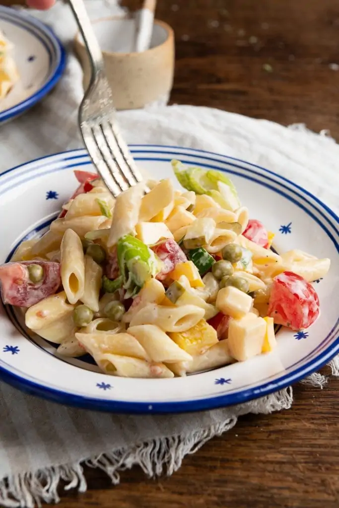 Vegetarischer Nudelsalat mit Penne, Erbsen, Paprika, Tomaten, Gewürzgurken und Käsewürfeln in cremigem Dressing auf einem Teller, ideal für ein kurzes Abendessen Gericht im Sommer.
