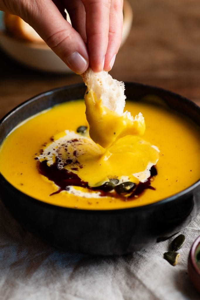 Ein Stück Brot geht in die kürbissuppe mit kartoffeln.