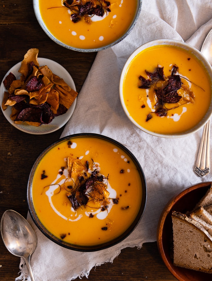 Drei Teller mit karotten ingwer suppe mit kokosmilch auf dem Tisch.