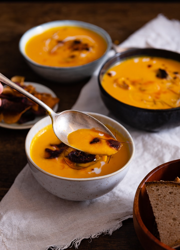 Ein Löffel mit karotten ingwer kokos suppe und einem Chilifaden.