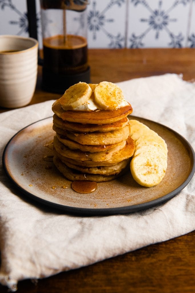 Die fertigen vegane Bananen Pancakes ohne Ei auf einem Teller mit Kaffee im Hintergrund.