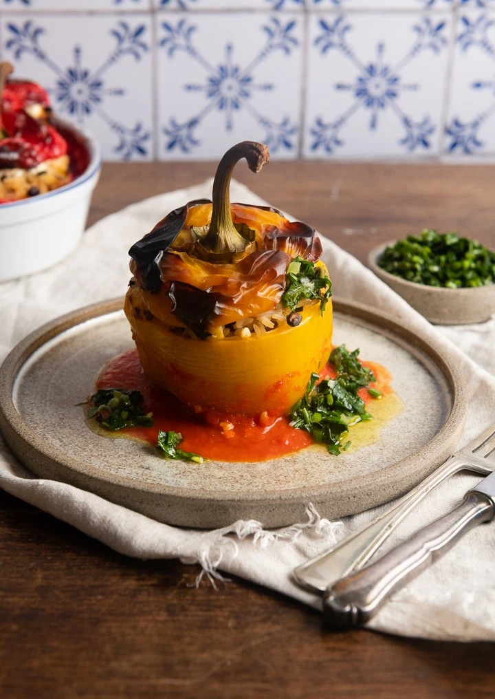 Eine gefüllte Paprika aus dem Backofen auf einem Teller mit Messer und Gabel daneben.