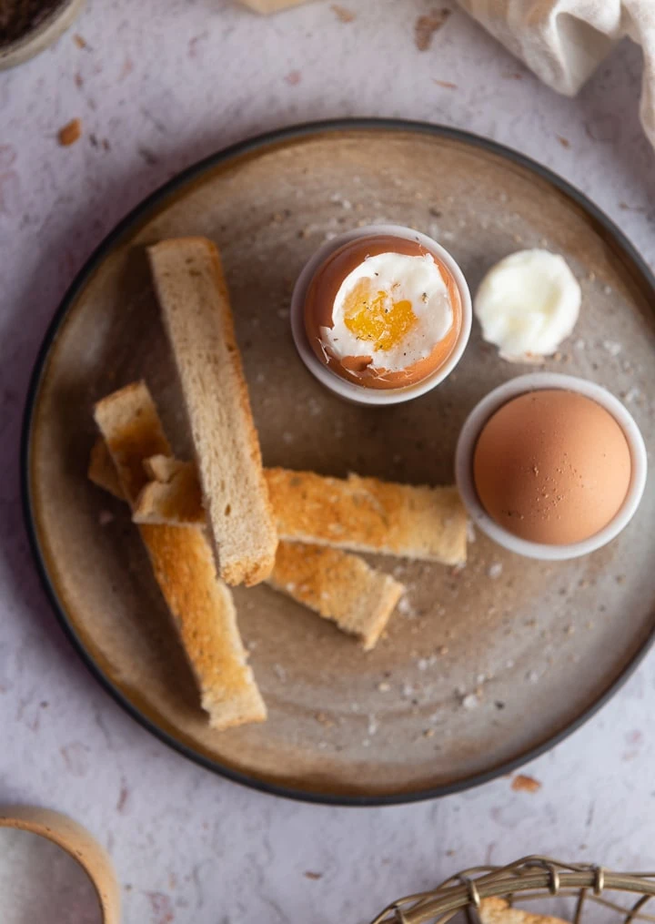 Ein weich gekochtes ei mit Toastbrot auf dem Teller.