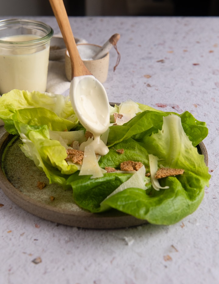 Caesar Dressing wird über einen Salat mit einem Löffel gegeben.