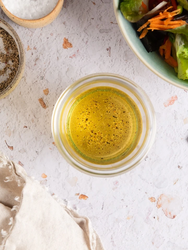 Das fertige Essig Öl Dressing neben einem Salat auf dem Tisch.
