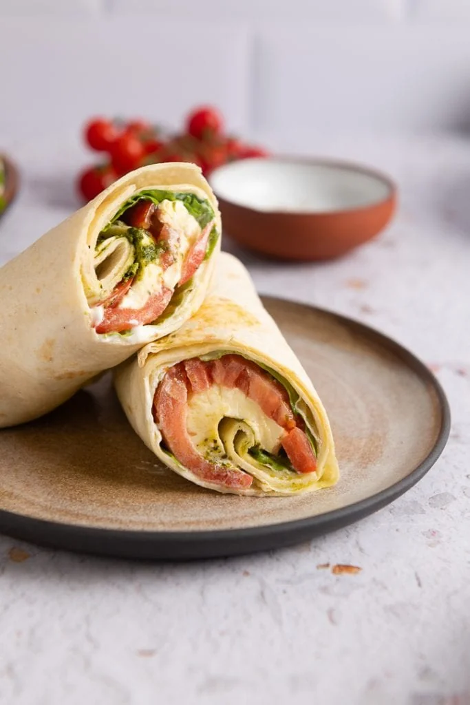 Halbierter vegetarischer Tomate-Mozzarella-Wrap, der die Füllung aus Tomaten- und Mozzarellascheiben, Pesto und Salat zeigt.
