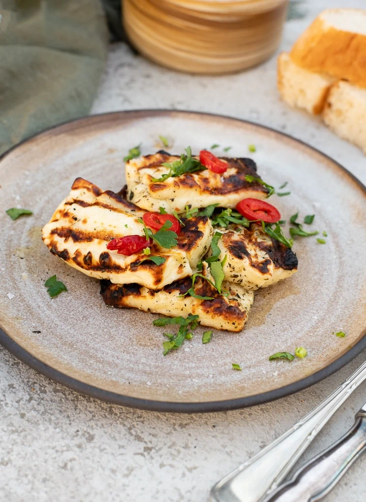 Gegrillte Halloumi-Scheiben mit deutlichen Grillstreifen, garniert mit frischen Kräutern und Zitronenspalten.