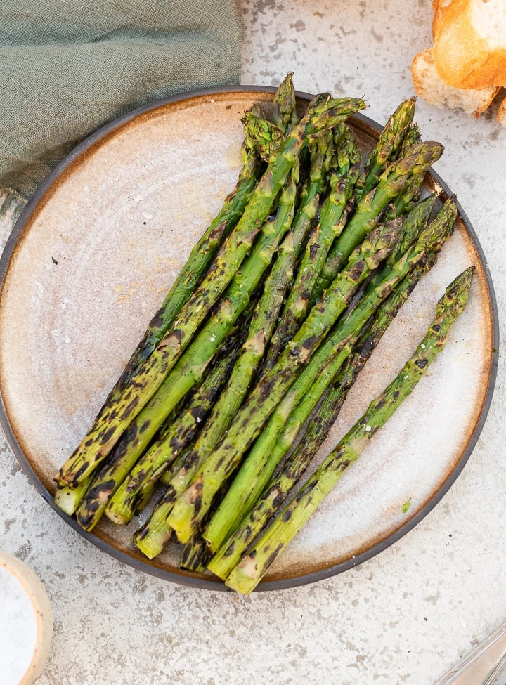 Grüner Spargel der direkt auf dem Grill gegrillt wurde, liegt auf dem Teller.