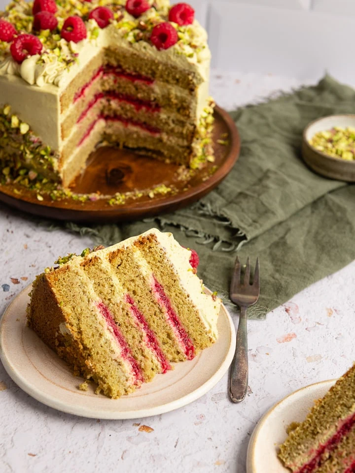 Ein Stück Pistazien Torte liegt auf einem Teller, daneben eine Kuchengabel.