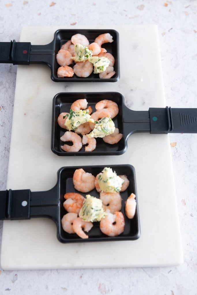Knoblauchbutter und Garnelen liegen in einem Raclette Pfännchen.