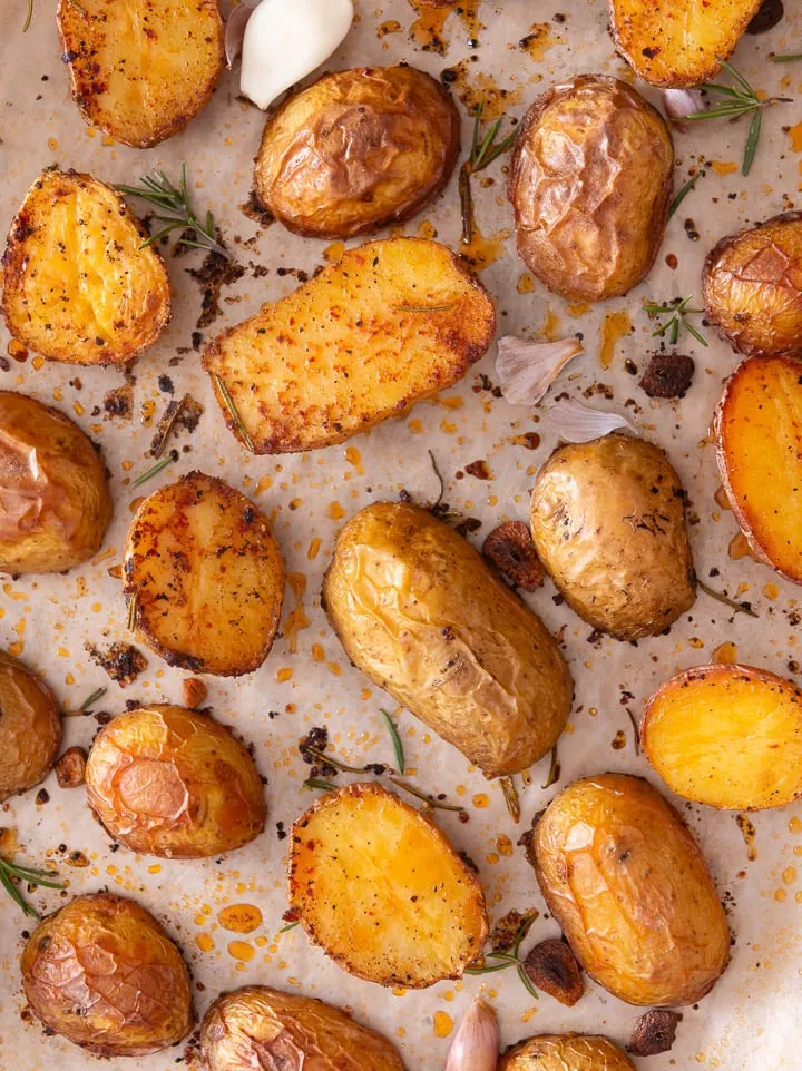 Ofenkartoffel liegen mit Rosmarin auf einem Backblech.