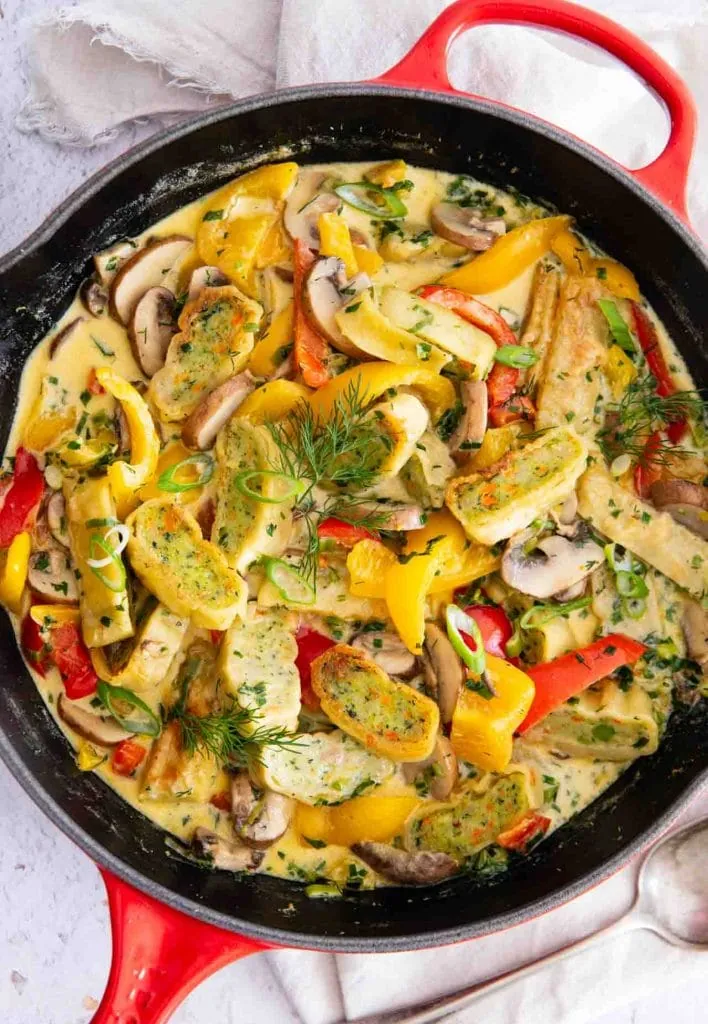 Angebratene vegetarische Maultaschen mit gelber und roter Paprika, Pilzen und Frühlingszwiebeln in cremiger Rahmsoße, garniert mit frischem Dill.

