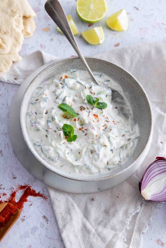 Der indischer Joghurt Dip steht mit einem Löffel drinnen auf dem Tisch.