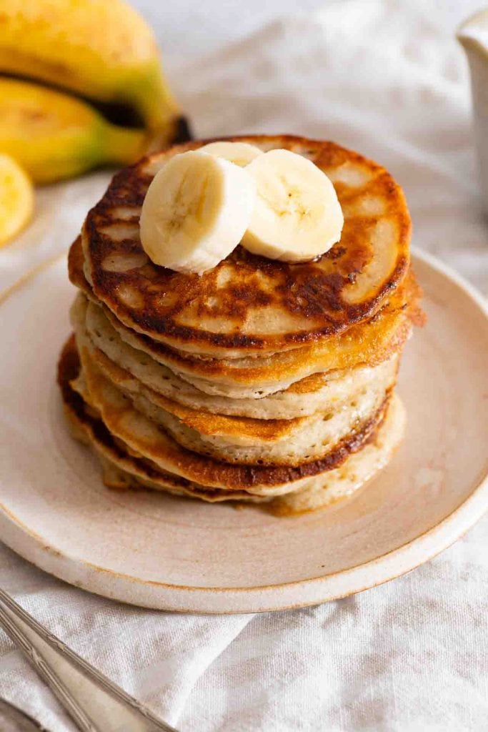 Bananen Pancakes ohne Ei auf einem Teller, oben darauf liegen Bananenscheiben.