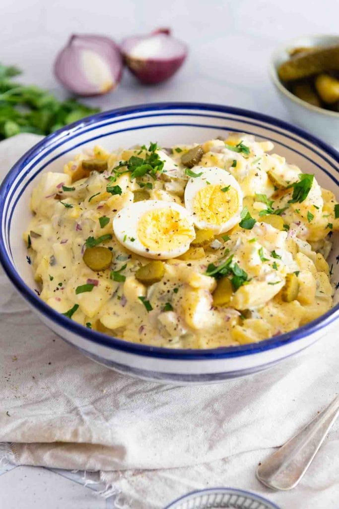 Ein Kartoffelsalat mit Mayonnaise in einer blau-weißen Schüssel.