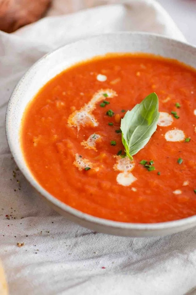 Tomatensuppe mit Reis in einer Schüssel, garniert mit Sahne und Basilikum.
