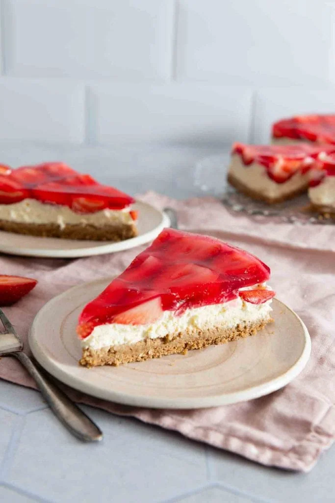 Ein Stück Erdbeerkuchen ohne Backen mit Keksboden auf dem teller, daneben liegt eine Gabel.