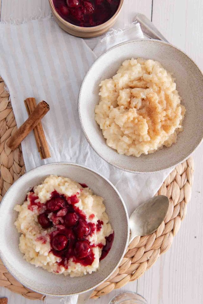 Zwei Milchreis mit Hafermilch stehen auf dem Tisch, einer von beiden hat Kirschen darauf.
