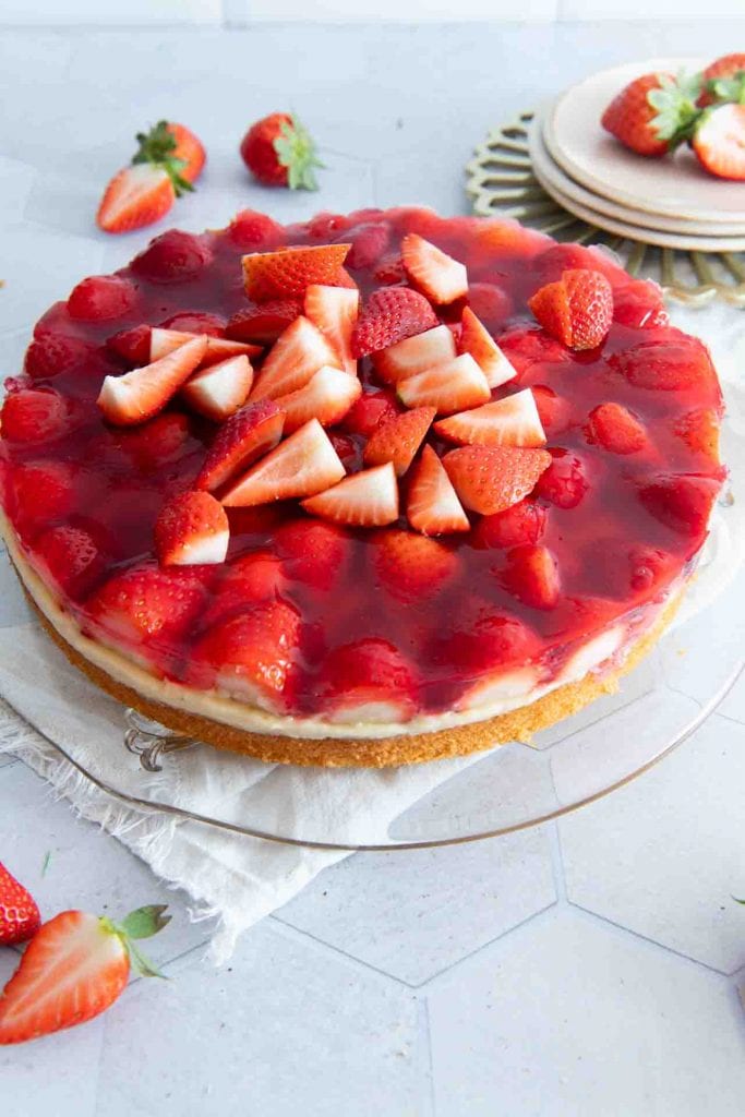 Ein Erdbeerkuchen mit Biskuitboden und Vanillepudding auf einer Kuchenplatte.