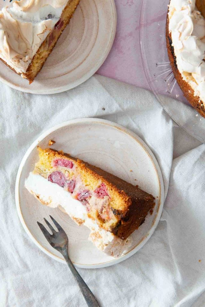 Ein Stück Rhabarberkuchen mit Baiser seitwärts auf dem Teller mit einer Kuchengabel.