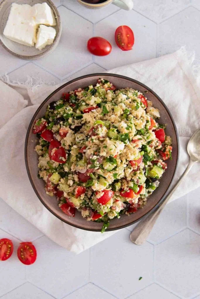Der Salatteller von oben, daneben liegt ein Löffel und ein paar Tomaten.