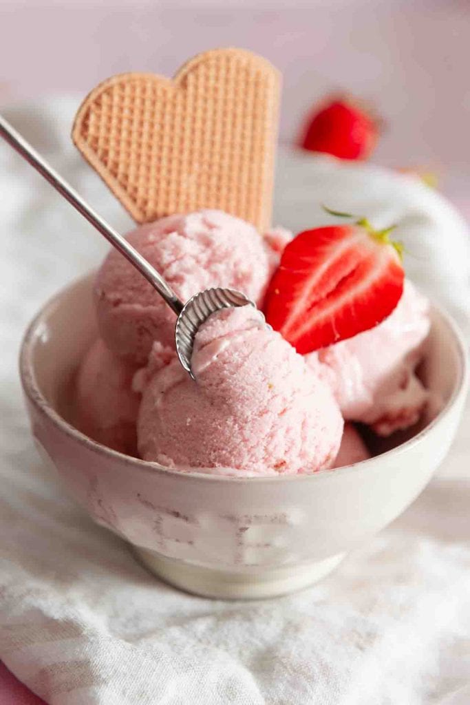 Ein Löffel nimmt Erdbeereis von dem Eisbecher mit Waffel auf.
