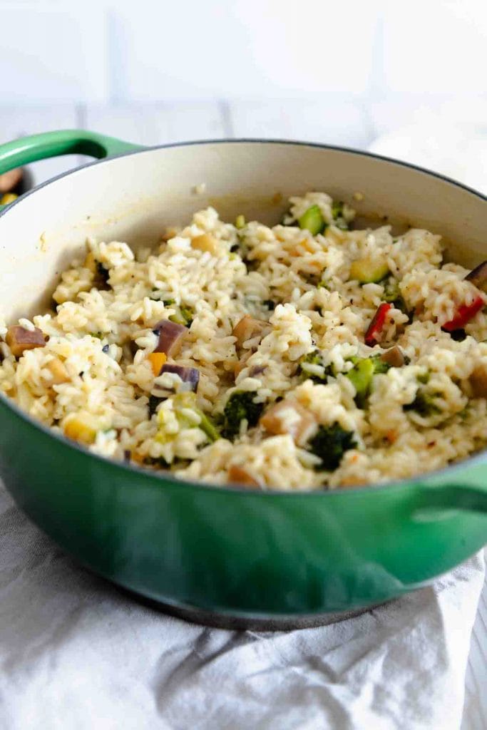 Ein Risotto mit Gemüse und Parmesan in einem grünem Topf.