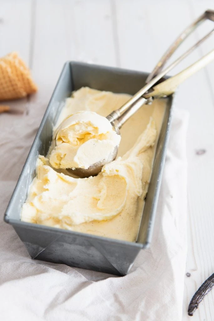 Eine Kugel Vanilleeis wird mit einem Eislöffel aufgenommen.