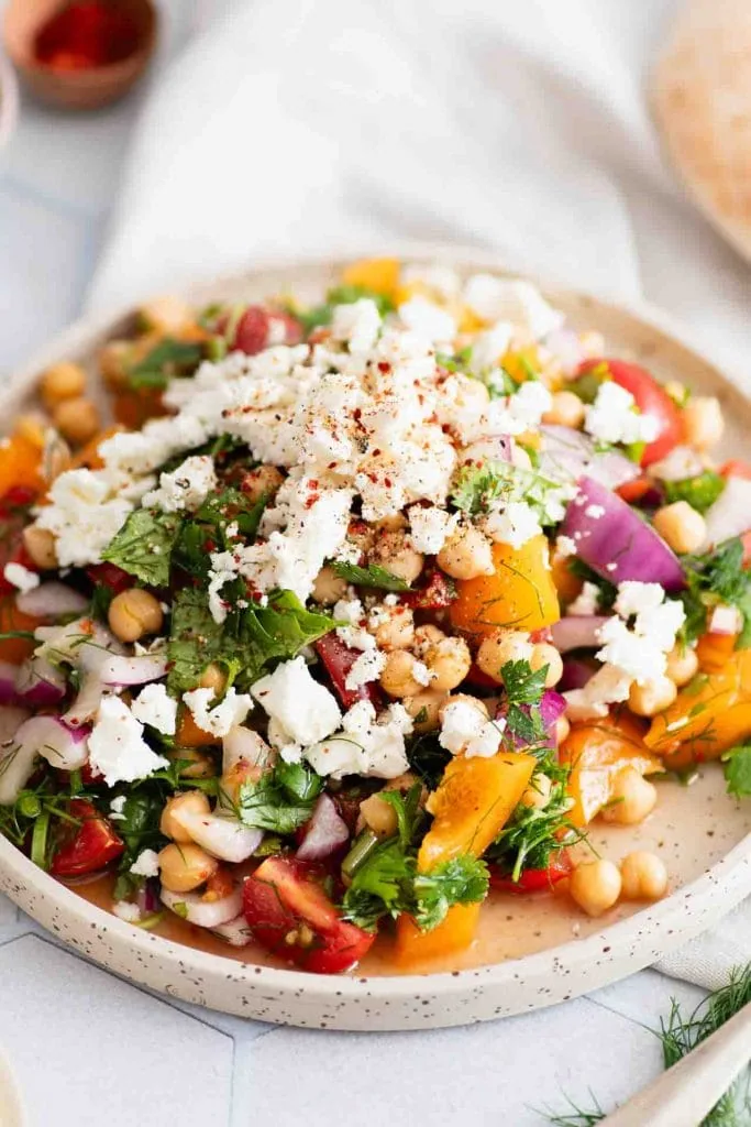 Frischer orientalischer Kichererbsensalat mit Feta, Tomaten, roten Zwiebeln, Dill und Petersilie, garniert mit Paprikapulver.
