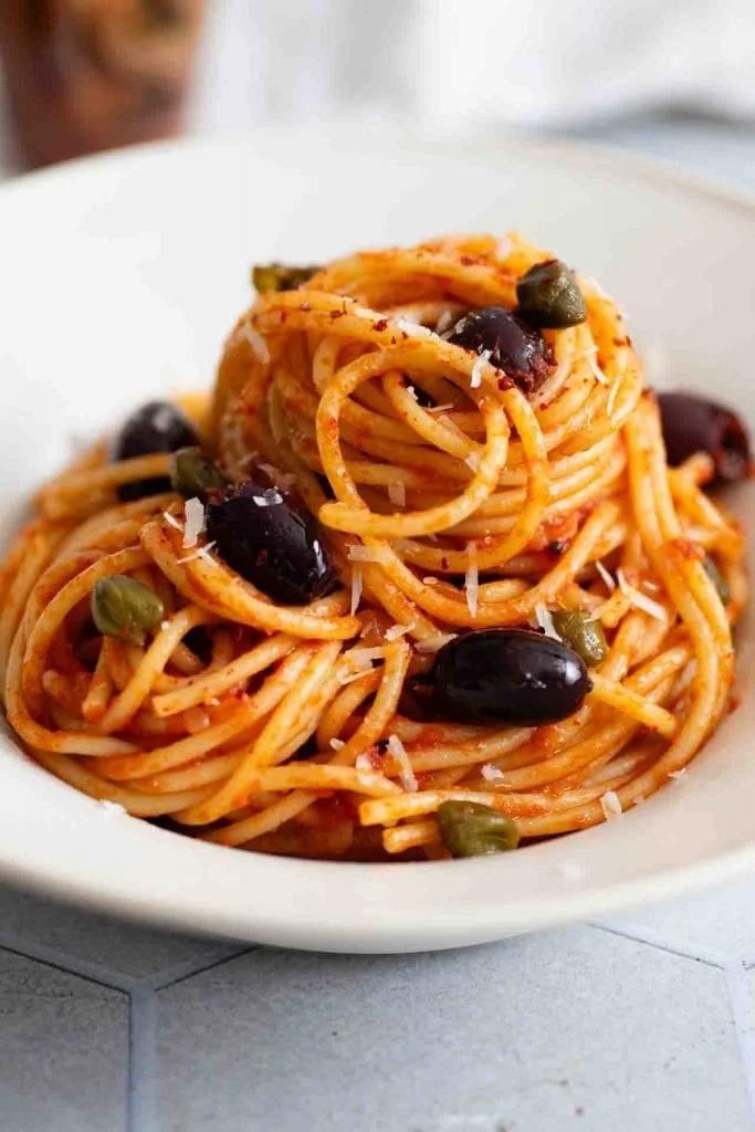 Spaghetti alla Puttanesca sind aufgerollt auf einem Teller.