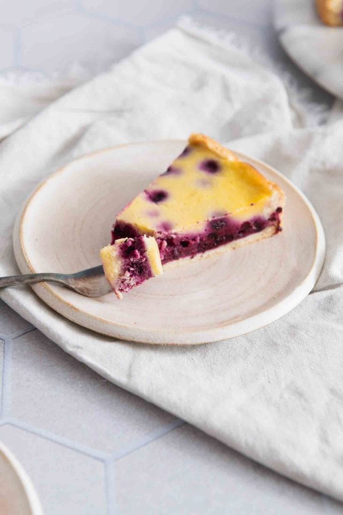 Eine Gabel nimmt ein Stück vom Heidelbeerkuchen mit Schmand und Pudding.