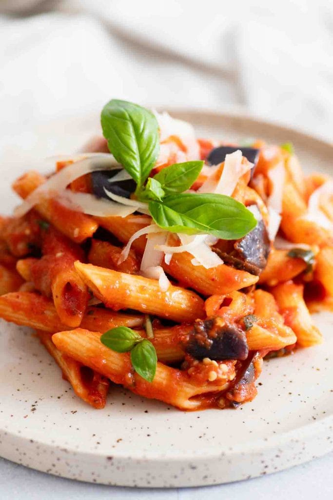 Ein Teller Pasta alla Norma mit einem Basilikumblatt auf den Nudeln.