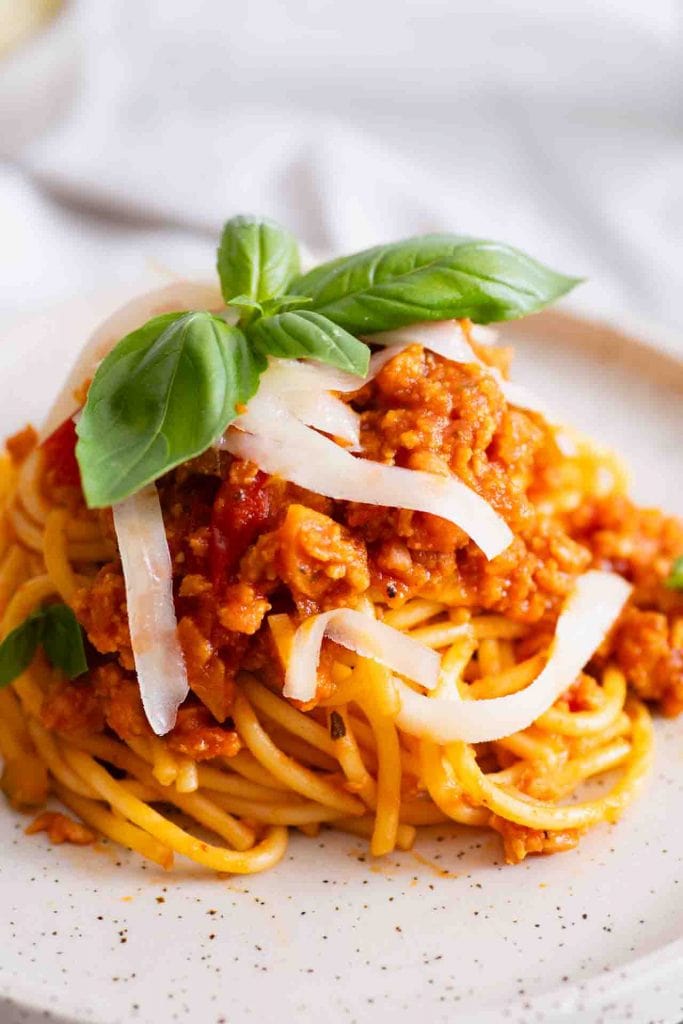 Ein Teller Spaghetti mit einer reichhaltigen vegetarischen Bolognesesoße (z.B. aus Linsen oder Sojagranulat), garniert mit gehobeltem Parmesan (oder veganer Alternative) und frischen Basilikumblättern