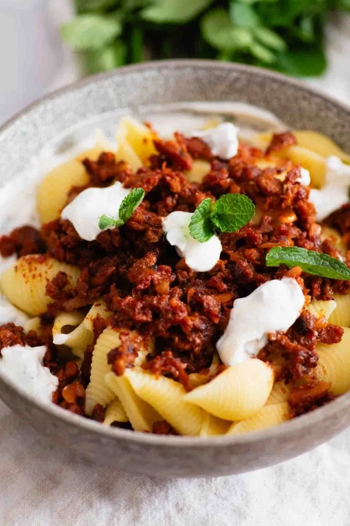 Türkische Pasta: Muschelnudeln (Conchiglie) mit einer würzigen Hackfleischsoße, garniert mit Klecksen von Joghurt und frischen Minzblättern, serviert in einer grauen Schale.