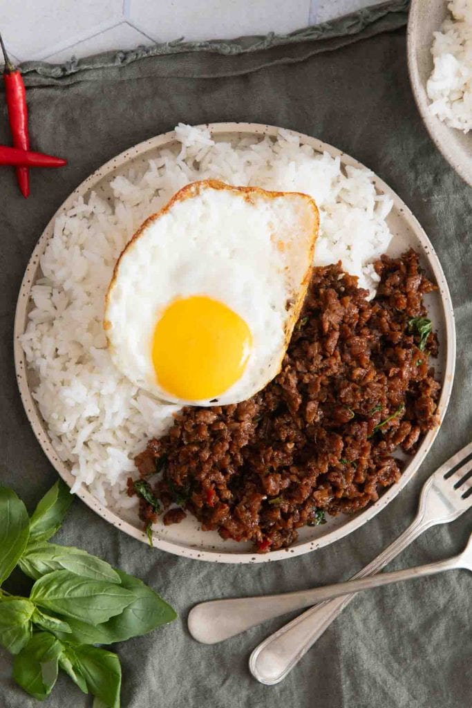 Pad Kra Pao: Gebratenes Veggie Hackfleisch mit viel heiligem Thai-Basilikum und Chili in einer würzigen Soße, serviert neben weißem Reis und getoppt mit einem Spiegelei.