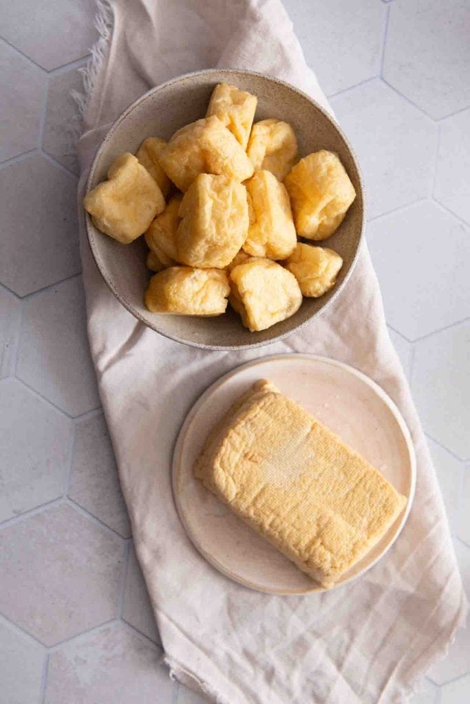 Goldbraune, frittierte Tofu-Puffs (Tofutaschen) in einer hellen Schale mit blauem Rand, einige aufgeschnitten zeigen die luftige Innenstruktur.