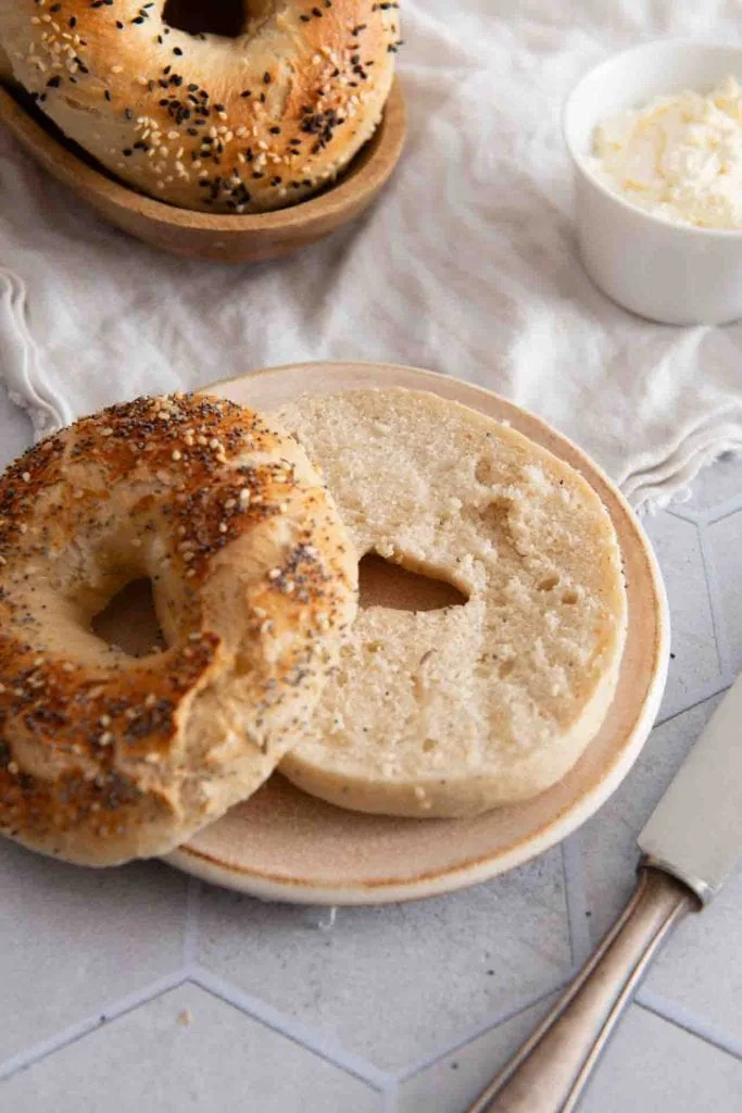 Neben einem angeschnittene Bagel, stehen weiter Bagel und Frischkäse.