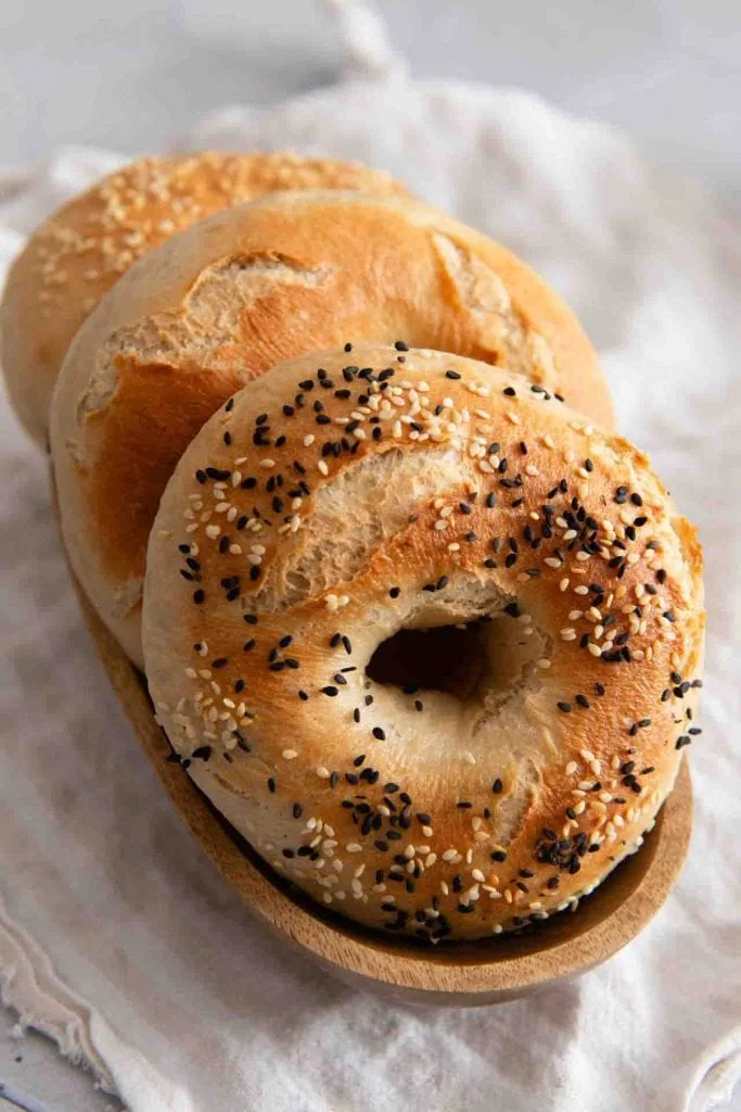 Drei selbstgemachte Bagels auf einem Holzteller.