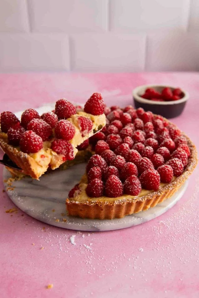 Ein Stück Himbeer Tarte wird von einer Kuchengabel aufgenommen.