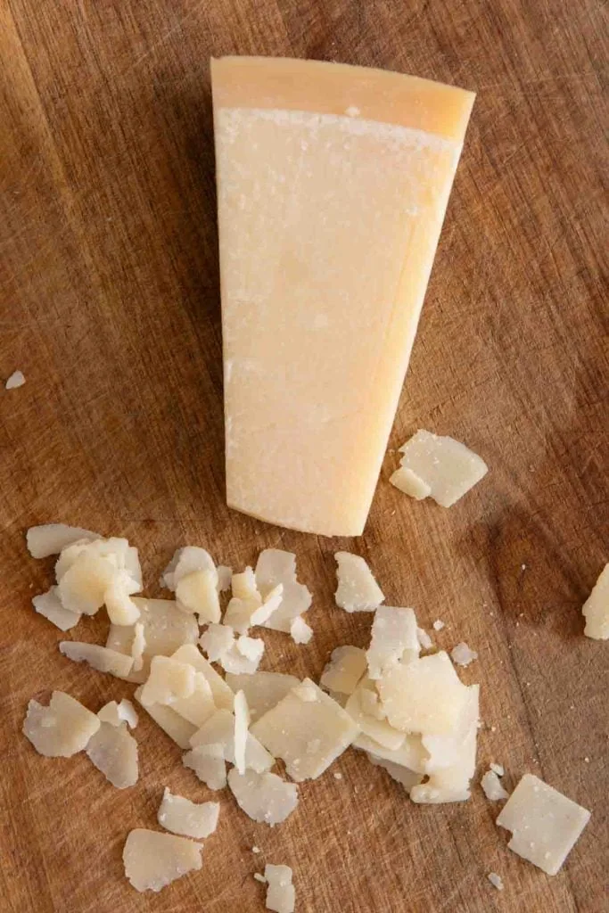 Ein Stück Grana Padano sowie einige Flocken davon liegen auf einem Brett.