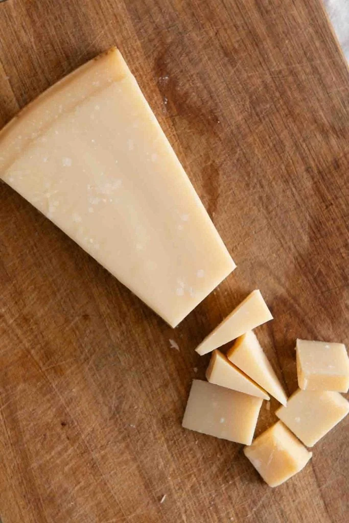 Ein Stück Parmigiano Reggiano liegt angeschnitten auf einem Holzbrett.