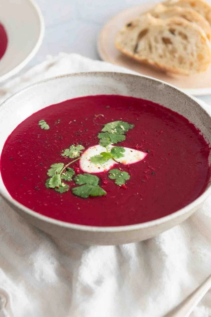 Eine Schüssel mit Rote Bete Suppe mit Ingwer ist mit einem Klecks Creme Fraice und Korianderblättern dekoriert.