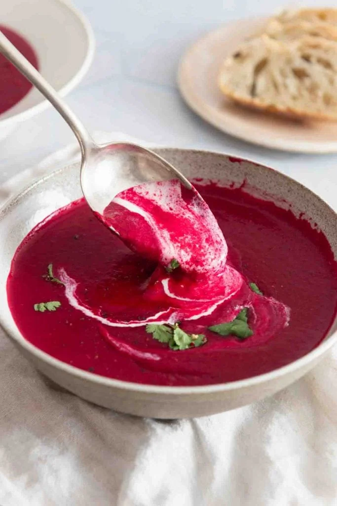 Ein silberner Löffel wird aus einer Schüssel mit Rote Bete Suppe mit Kokosmilch gehoben. Die Suppe tropft cremig vom Löffel.