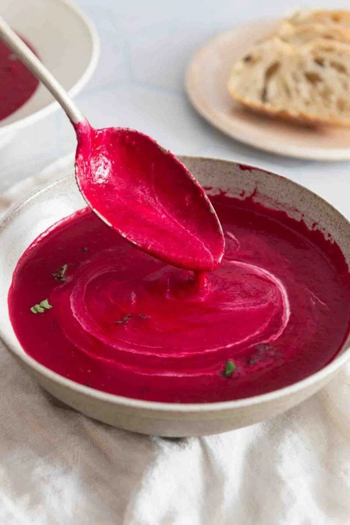 Rote Bete Suppe mit Ingwer tropft cremig von einem silbernen Löffel.